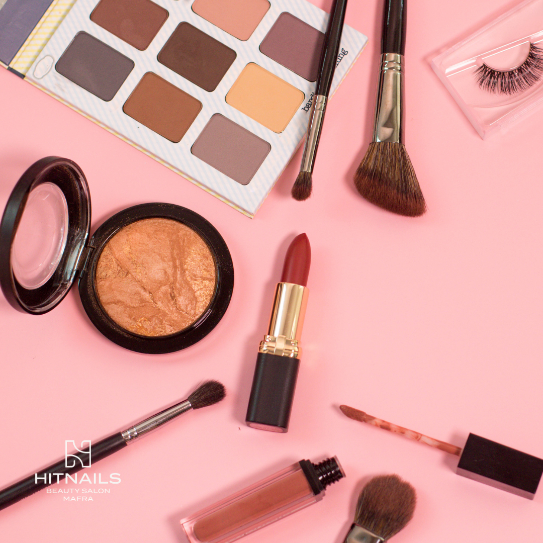 Paleta de sombras, pincéis, batom e pestanas postiças sobre fundo rosa