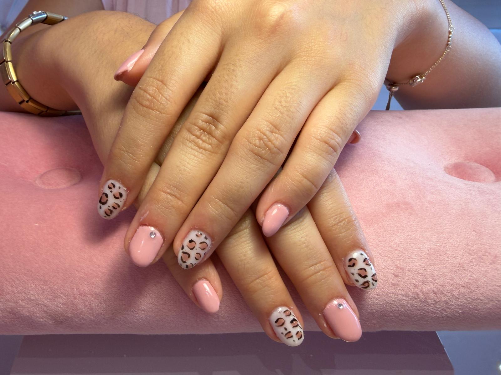 Unhas curtas em rosa nude com nail art de leopardo em preto e pedrinha na anelar, feitas no Hit Nails Mafra