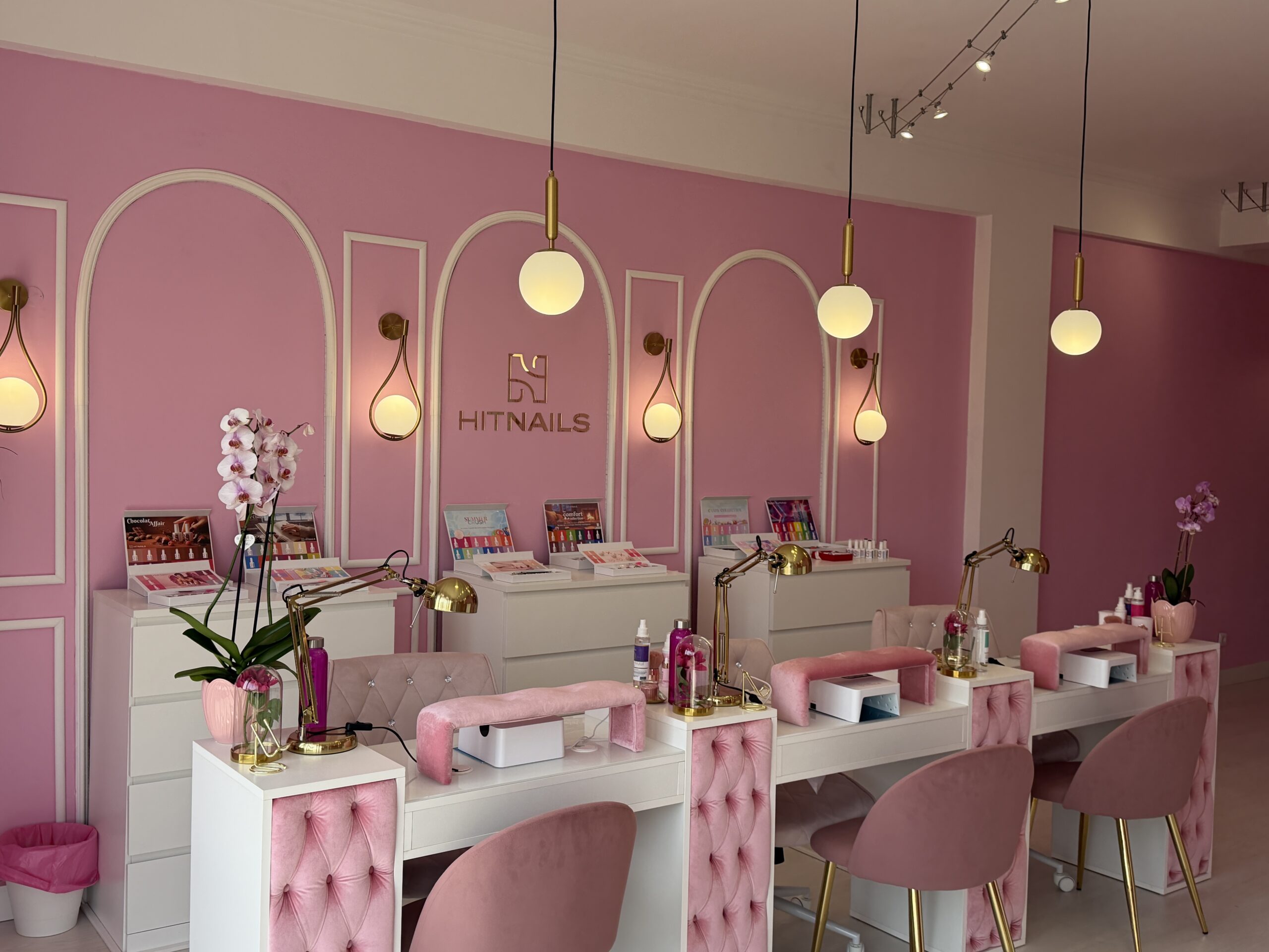 Zona de manicure do Hit Nails Mafra, com arcos na parede, cadeiras em veludo rosa e candeeiros dourados