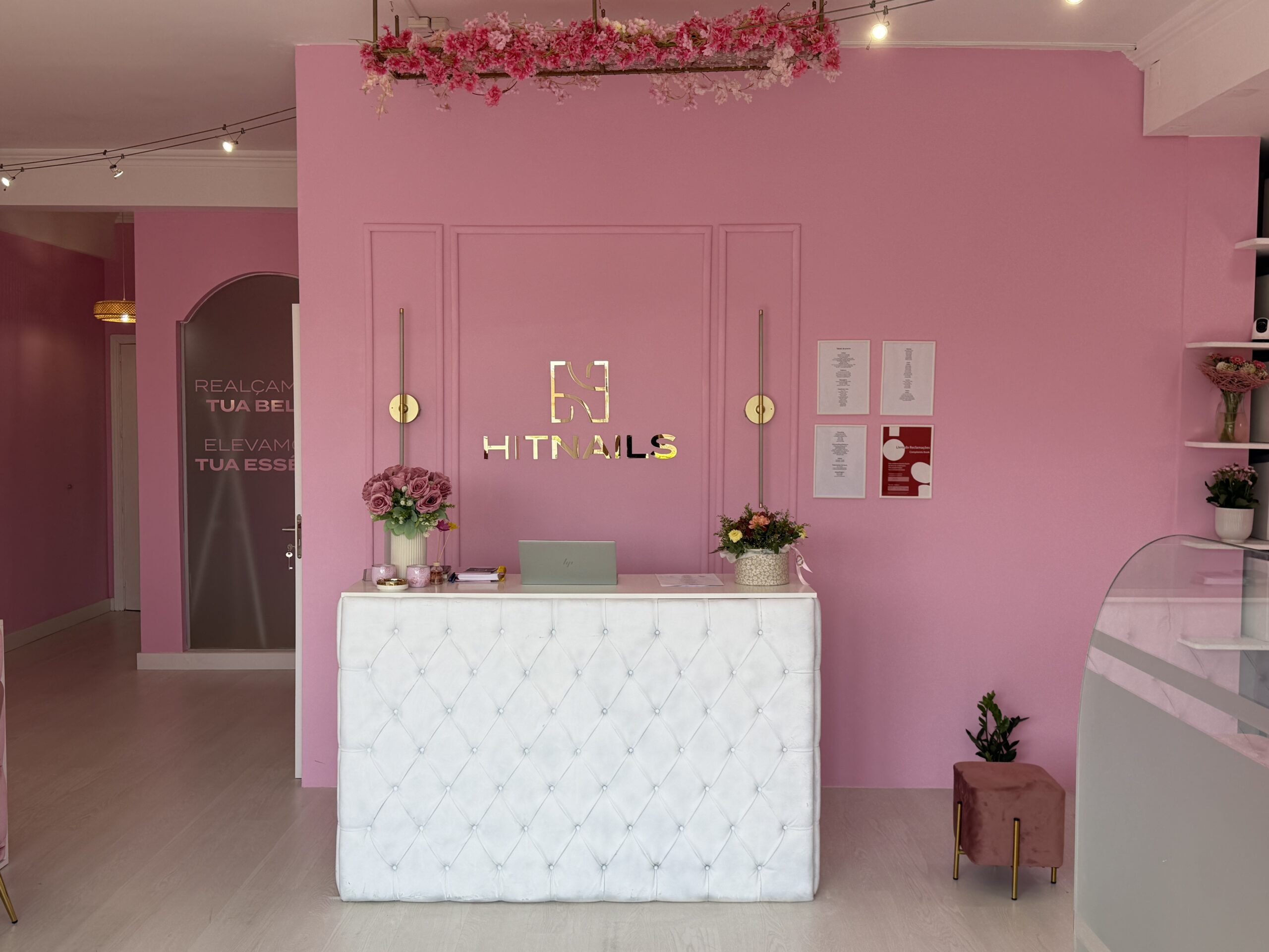 Receção do Hit Nails Mafra, com o logótipo dourado na parede rosa e o festão de flores